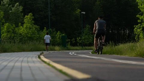 A cyclist and a runner move along a bike path Stock Photos