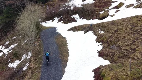 Cyclist approaching snow blocked mountain road drone follow Видео 333070429