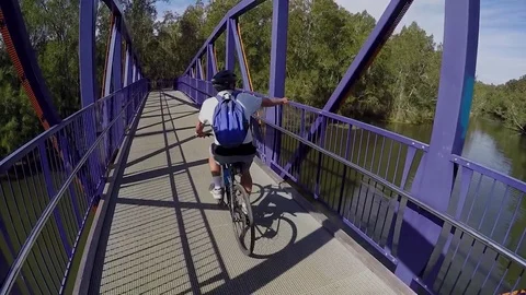 Cyclist with a backpack rides over a bridge in a nature reserve. Видео 78733503