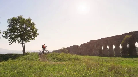 Cyclist with bike reads map for direction in front of ancient roman aqueduct in Vídeo Stock 84909155
