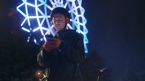 Cyclist Checking Smartphone by Amusement Park Ferris Wheel Lights 库存影片 345709204