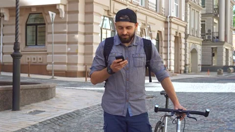 Cyclist checks cellphone while standing on a charming city street Stock-Footage 311945195