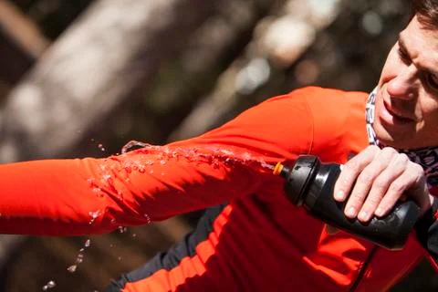 Cyclist dunking his red jacket with the water pot Stock Photos