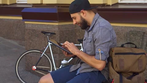 Cyclist engrossed in tablet use on a vibrant city street Stock Footage 311944599