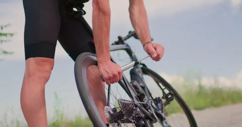 Cyclist fixes flat tire on road bike while riding through nature on sunny day Stock Footage 339496981