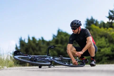 Cyclist fixes flat tire on a road bike during a cycling trip in the countryside Stock Photos
