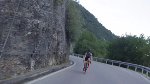 A cyclist goes down a road and passes a mountain bridge Stock Footage 78156111