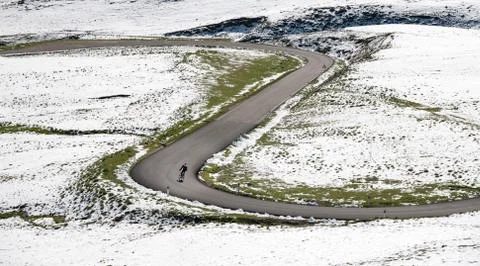 Cyclist goes downhill along a mountain road in a snowy landscape Stock Photos