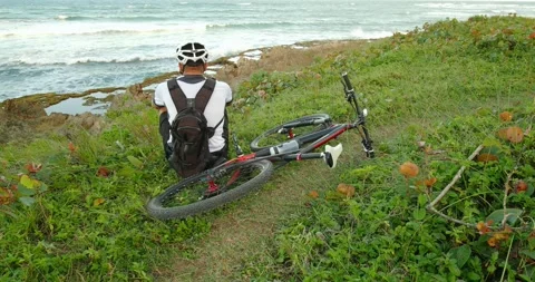 Cyclist man with bicycle sitting next to ocean looking away. Stock Footage 231267992