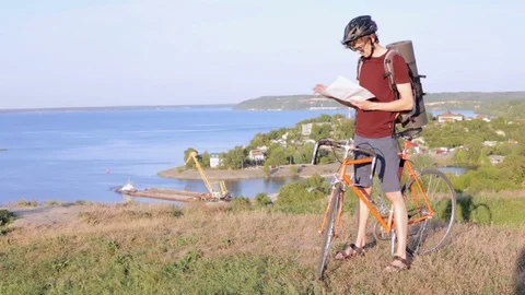 Cyclist on the mountain top is considering a road map Stock Footage 82334344