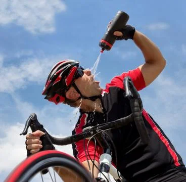 Cyclist refreshes from a bottle while riding a bicycle Stock Photos