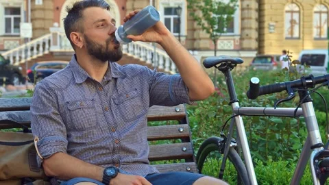 Cyclist refreshes with water while resting on a bench Stock Footage 311937658