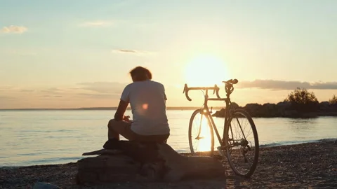 Cyclist resting at sunset on beach Stock Footage 315521630