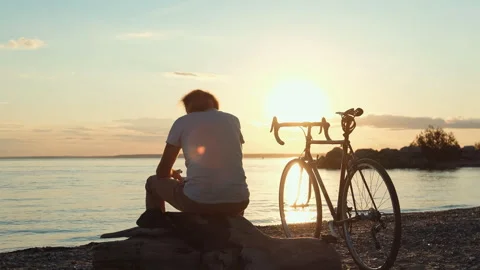 Cyclist resting at sunset on beach Stock Footage 315522134