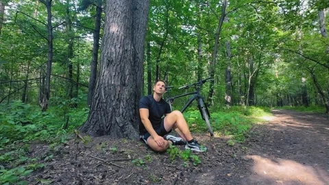 Cyclist resting under tree in sunny forest Stock Footage 315408029