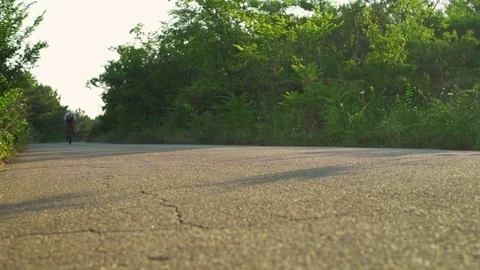 Cyclist ride sunny asphalt road in the forest sunrise helmet rapid slow motion Stock Footage
