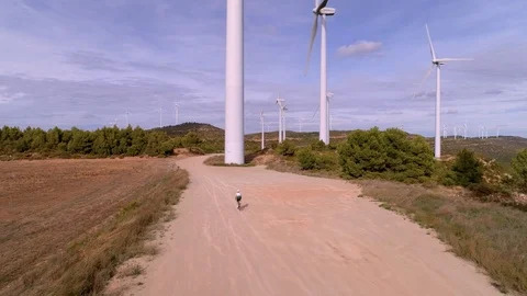 Cyclist rides between turbine wind farm at sunset Video stock 123080697