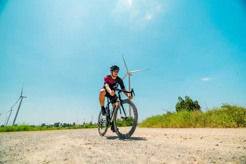 Cyclist rides on a dirt path surrounded by wind turbines on a clear sunny day Stock Photos
