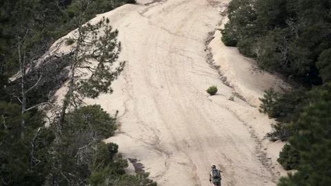 A cyclist rides up a steep dirt path next to a forest Stock Footage 91277495