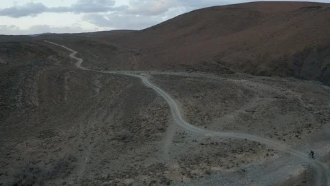 A cyclist rides uphill through a desolate but beautiful rocky, desert landscape. Stock Footage 127023426