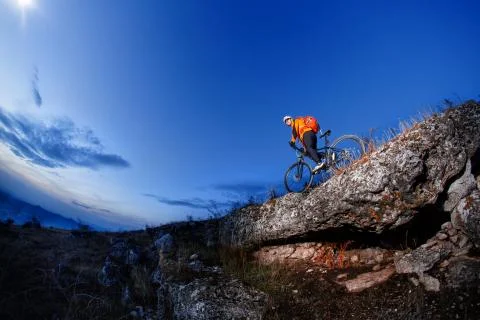 Cyclist Riding the Bike Down Hill on the Mountain Rocky at Sunset. Stock Photos