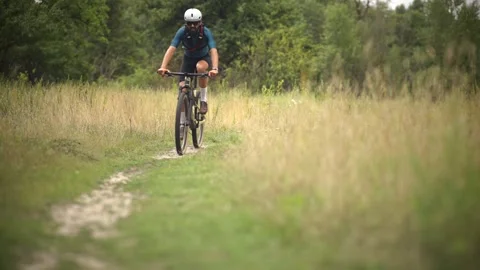 Cyclist riding on grassy trail through forest landscape Stock Footage 313951403