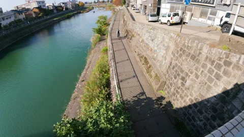 Cyclist riding on a riverside path in a quiet neighborhood of Kanazawa Stock Footage 331955130