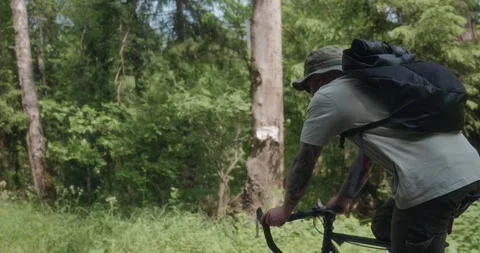 Cyclist riding through forest, camera zooms out from close to wide Stock Footage 311919744