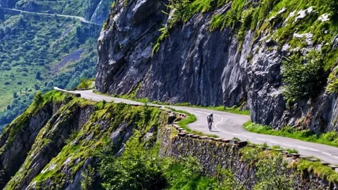 Cyclist riding winding cliffside mountain road at Col d'Aubisque France Stock Footage 341536635