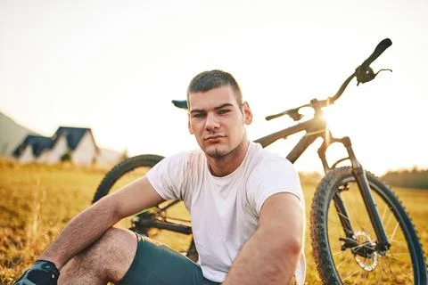 The cyclist sits in a meadow while resting from a strenuous ride on mountain  Stock Photos