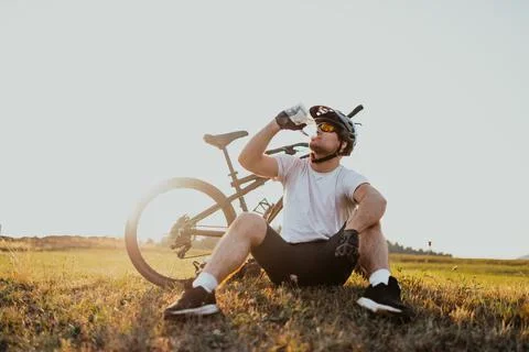 The cyclist sits in a meadow while resting from a strenuous ride on mountain  Stock Photos