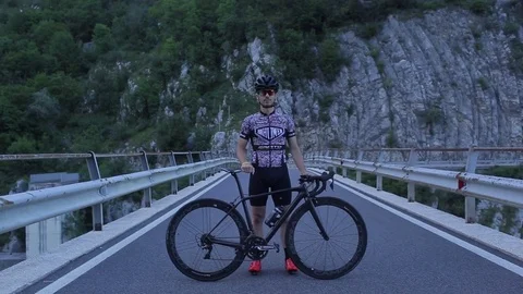 A cyclist is standing on a mountain bridge before dawn Stock Footage 78184689