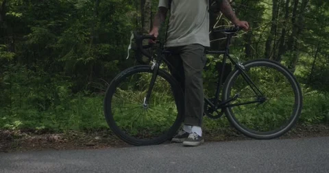 Cyclist standing on roadside in forest, face not visible Stock Footage 311934878