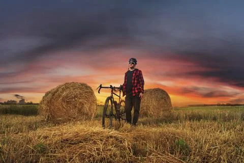 Cyclist stands with his bicycle in the field with haystacks at sunset. Stock Photos