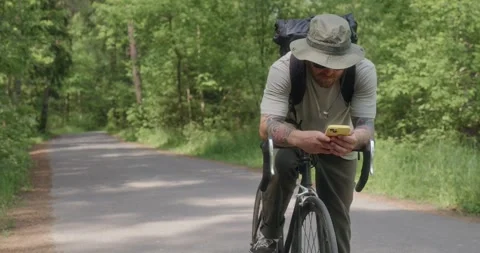 Cyclist stops on forest road to check map on phone Stock Footage 311918576