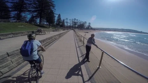 Cyclist tracking shot along beach path passing a cafe and people. Video stock 89734138