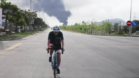 Cyclist trains on track under dramatic sky with smoke billowing in distance. Stock Footage 285587522