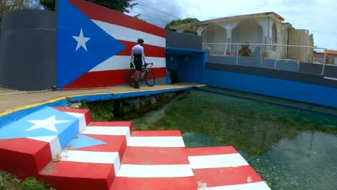Cyclist Walking on a Path next to a Spring, Wall with Puerto Rico Flag Desig Stock Footage 130339530