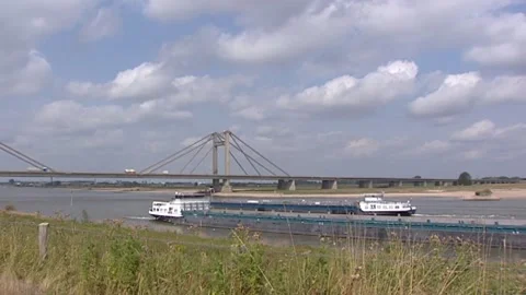 Cyclists across the river dike + pan toll bridge Prince Willem Alexander Stock Footage 166566612