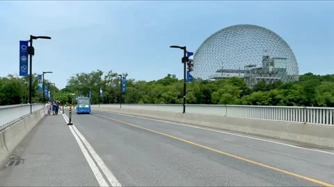 Cyclists and a shuttle bus on a bridge with the Biosphere dome in the background Stock Footage 346989310