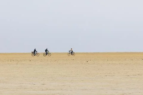 Cyclists approaching to cross paths on a vast empty beach Stock Photos