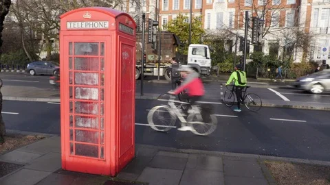 Cyclists in a cycle lane go past a British phone box in the rain 스톡 동영상 102719087