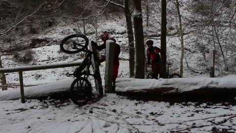 Cyclists emerge from snowy forest path with bicycles Stock Footage 83409161