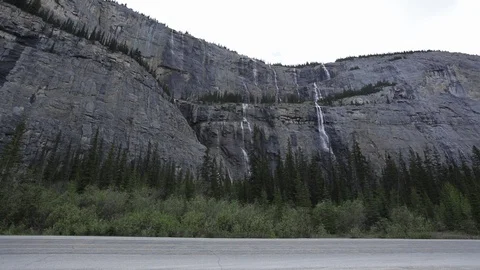 Cyclists pass a cliffside waterfall on a tandem bike in Alberta Stock Footage 90875525
