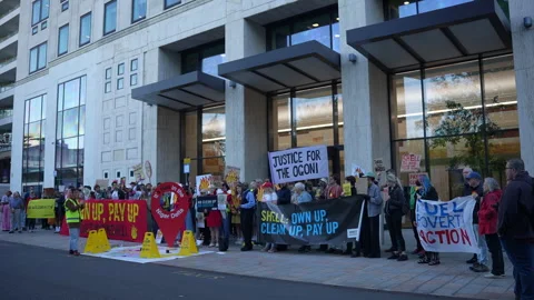 Cyclists Pass By People Holding Placards And Banners On A Protest Outside Shell Stock Footage 310536538