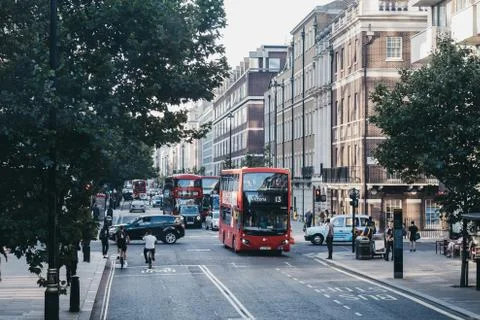Cyclists, red double decker buses and taxis on a street in London, UK. Stock Photos