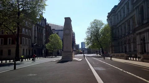 Cyclists riding pass the Cenotaph on an empty Whitehall street.  Slow motion Stock Footage 213155397
