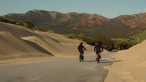 Cyclists riding through sand dunes with mountain view Stock Footage 308877322