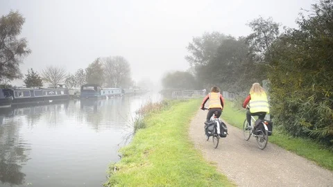 Cyclists on towpath alongside Kennet Canal, moored houseboats, fog Stock Footage 100993469