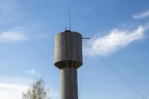 Cylindrical concrete water tower structure with ladder, blue base, outdoors Stock Photos